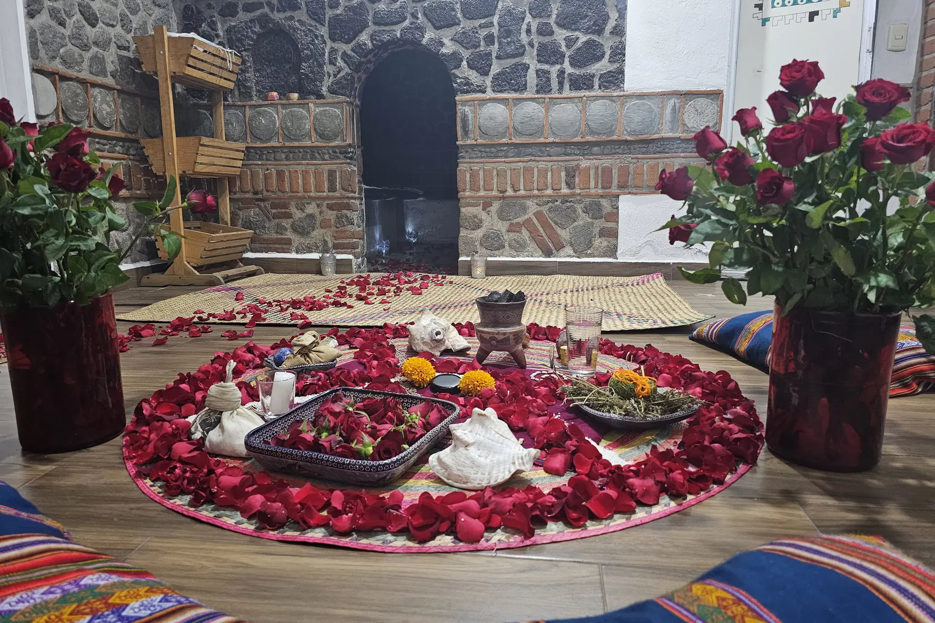 Altar de rosas rojas sobre círculo de pétalos, con la entrada del temazcal al fondo