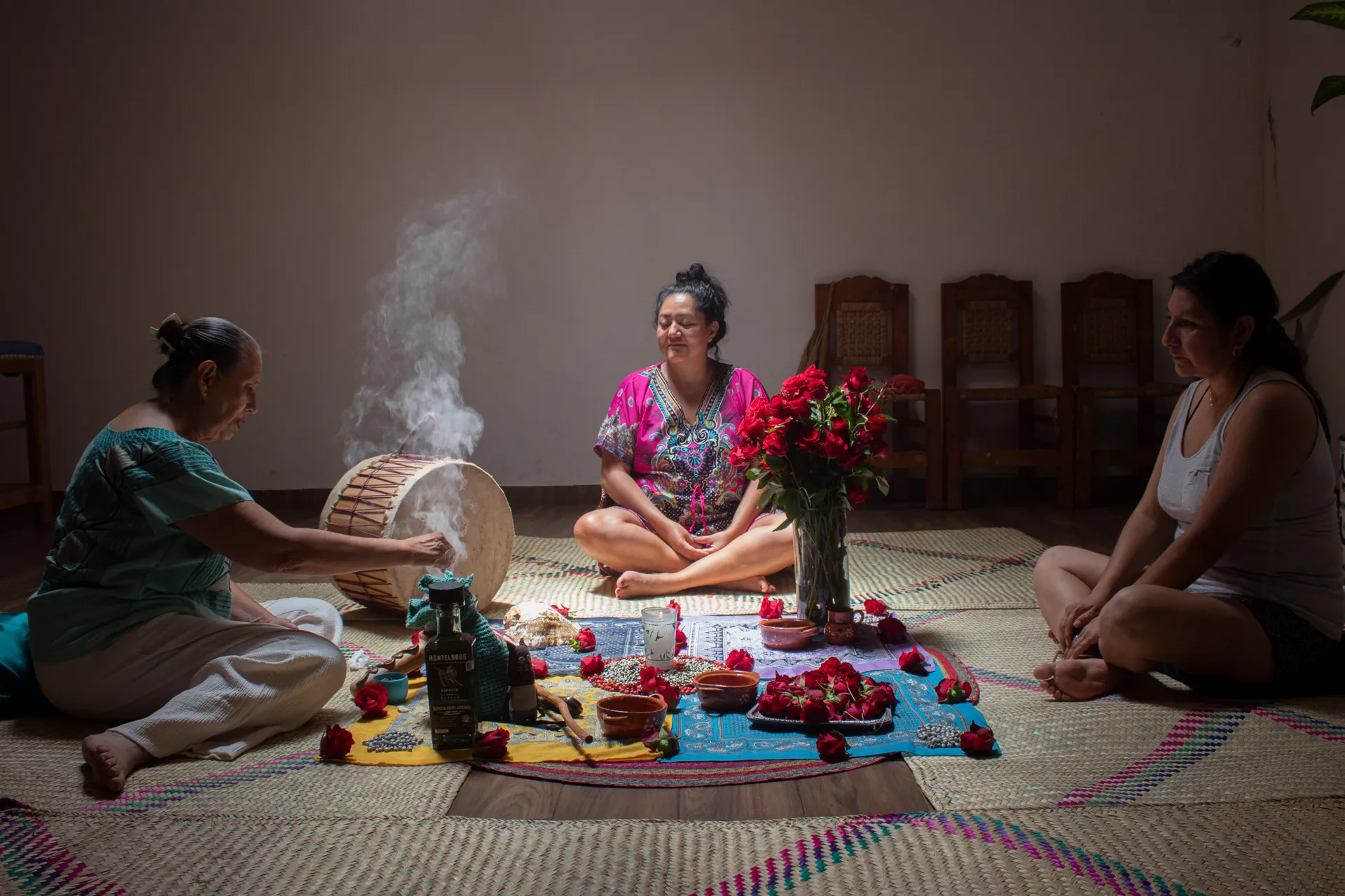 Ceremonia íntima en el salón: mujeres sentadas en petates alrededor del altar de rosas mientras sube el humo de copal