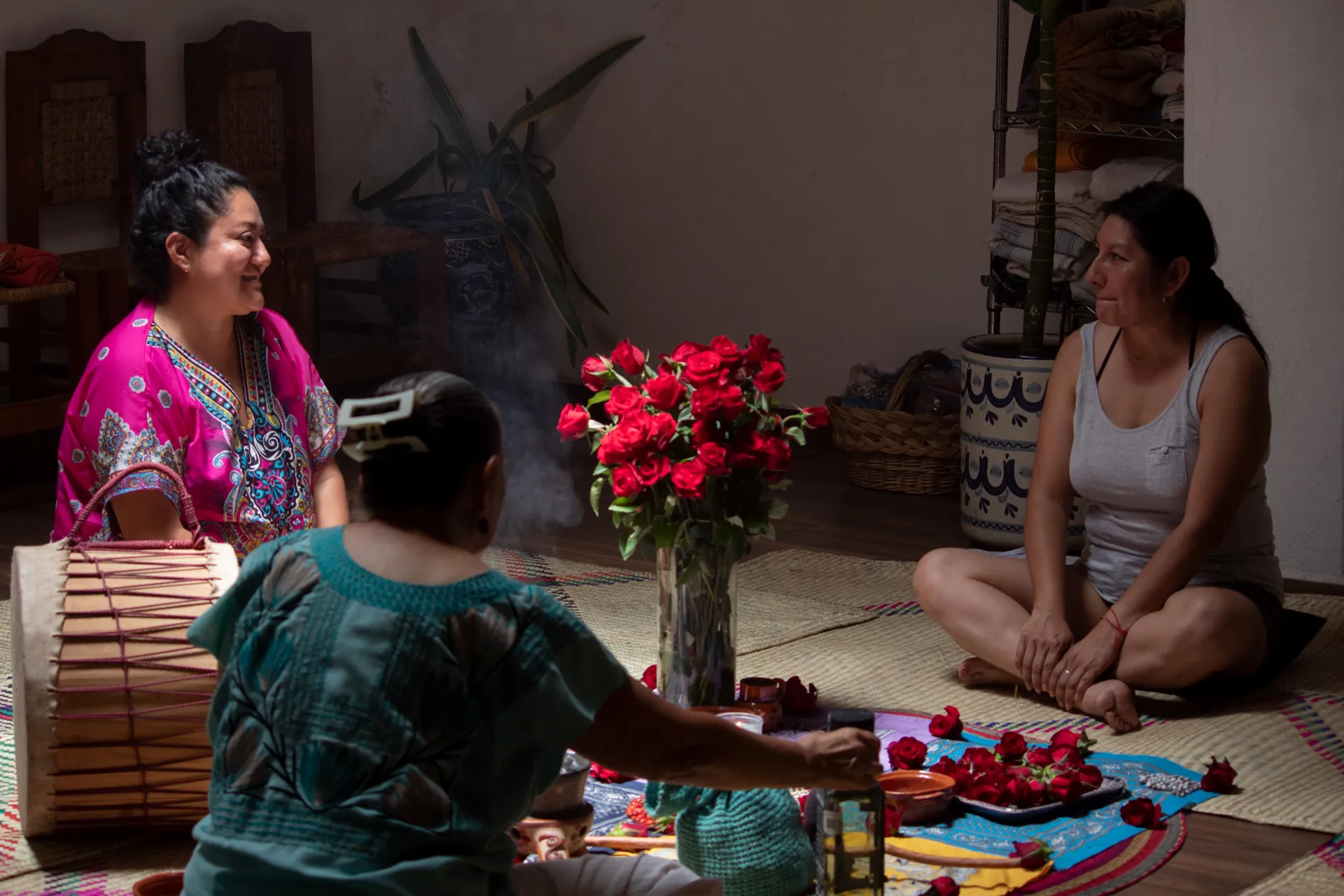 Ceremonia íntima en el salón: mujeres sentadas en petates alrededor del altar de rosas mientras sube el humo de copal