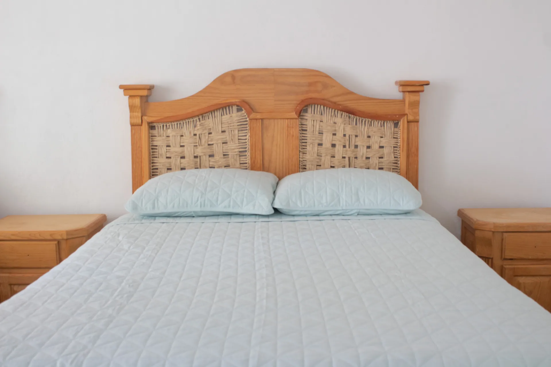 Cama con cabecera de madera tallada y colcha azul claro