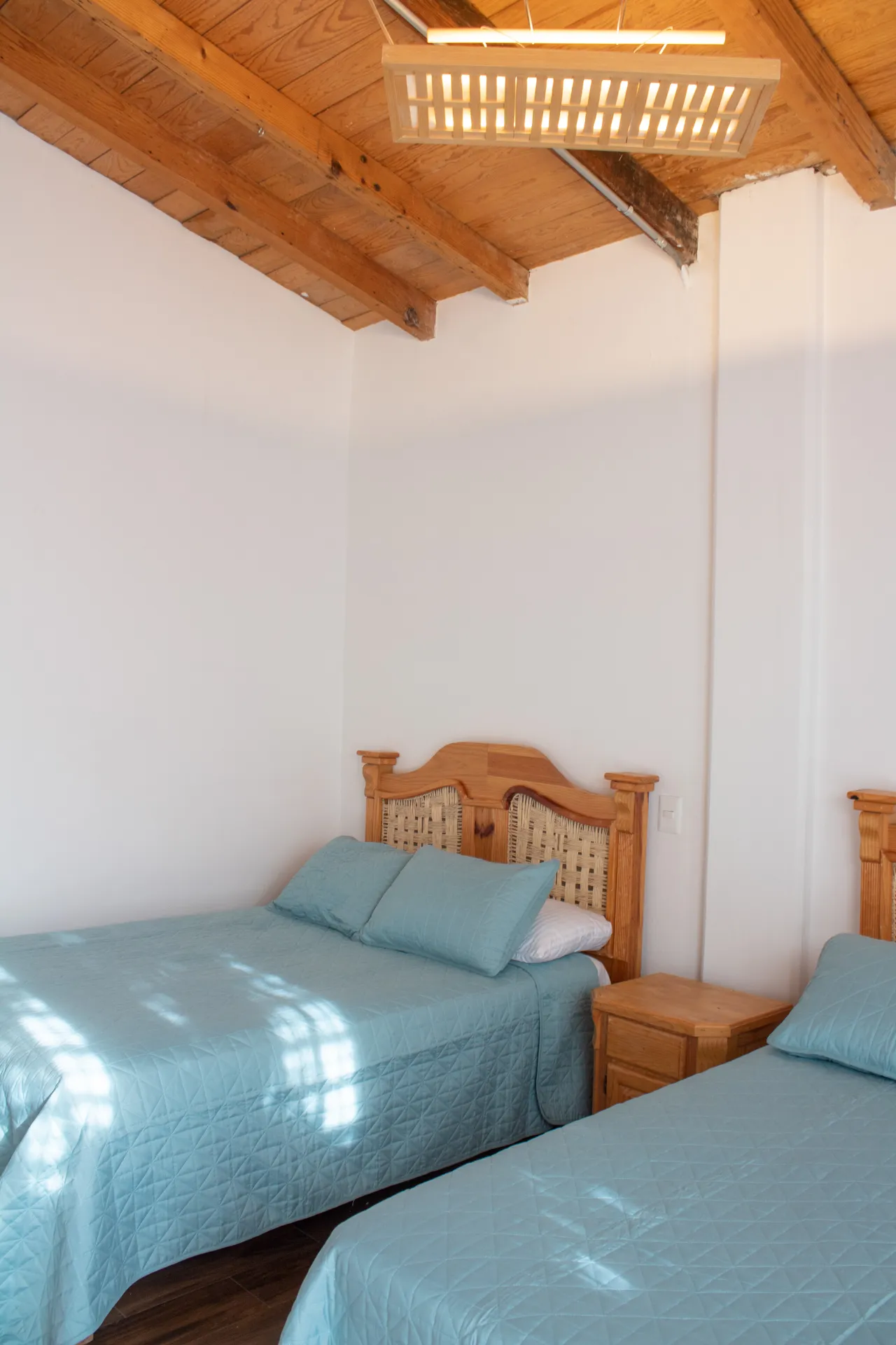 Habitación con techo de vigas de madera, lámpara de palma y camas gemelas