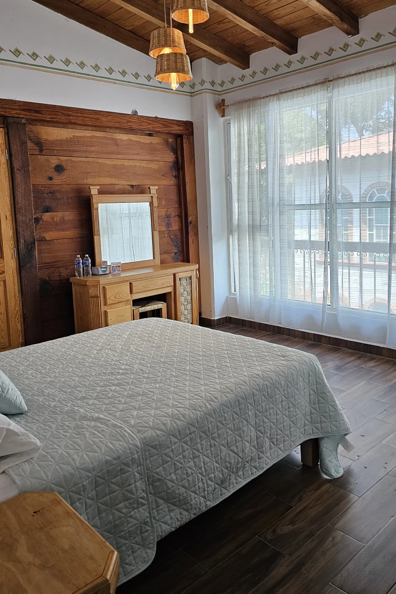 Recámara con muro de madera, tocador y ventanal con cortinas claras