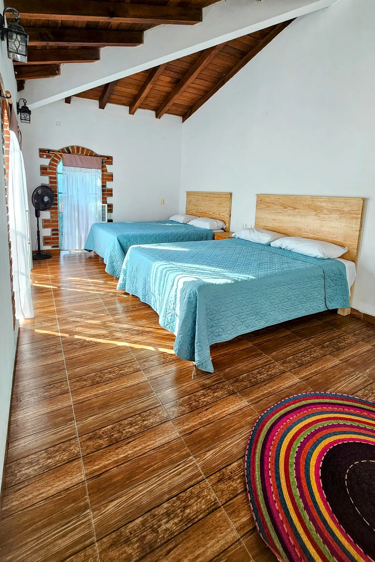 Recámara con dos camas de colchas turquesa, techo de vigas y tapete de colores
