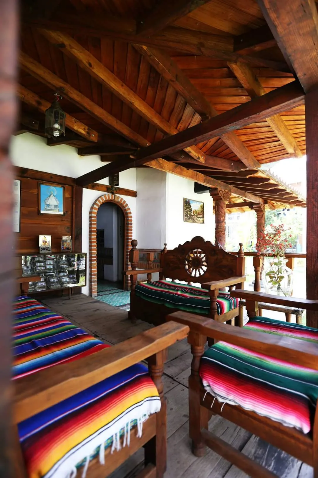 Terraza techada con vigas de madera, bancas talladas y sarapes de colores