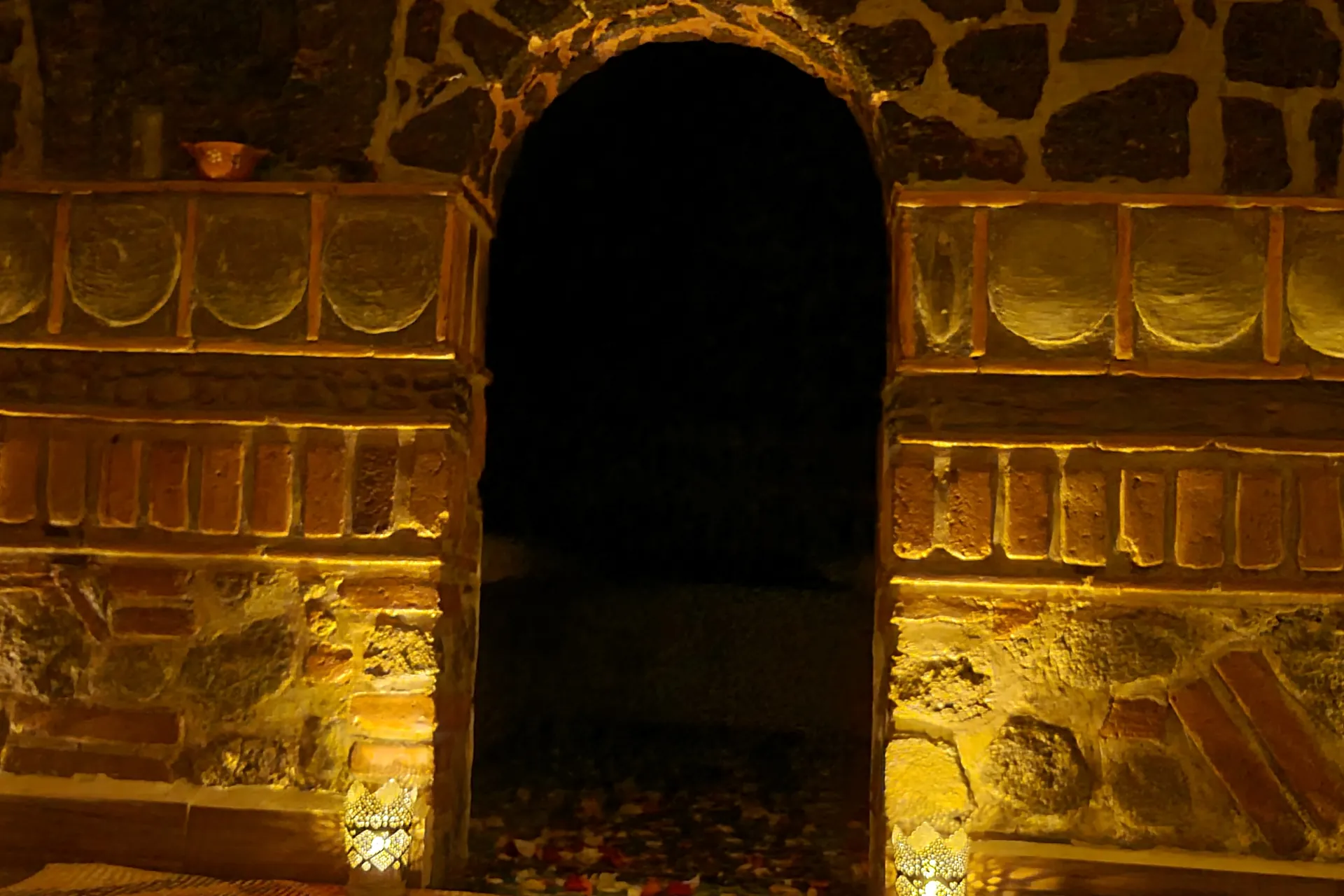 Portal de piedra volcánica y ladrillo del temazcal, iluminado con velas en la penumbra